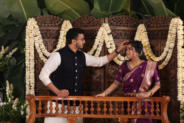 Akanksha and Kushal in Indian wear by a flower-covered wooden backdrop