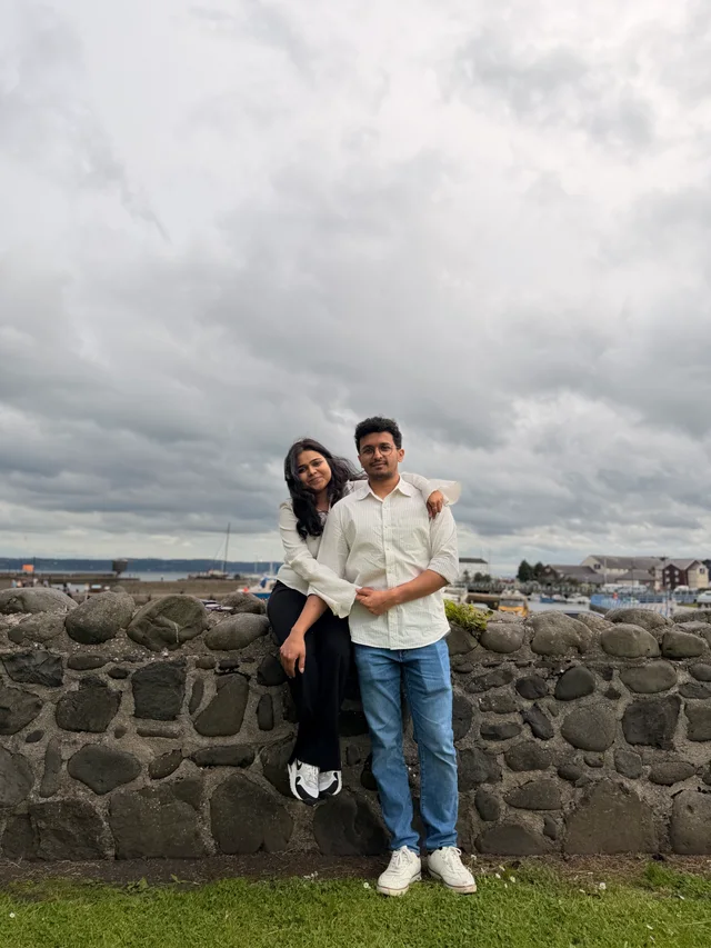 Akanksha and Kushal posing on a stone wall under a cloudy sky